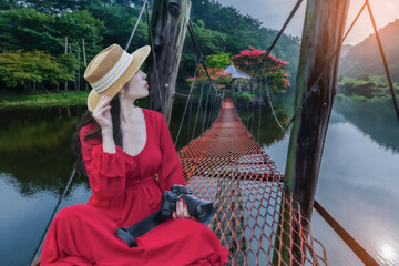 .Asian woman sits on a red bridge leading to an island in the middle of the water with colorful flowers. - 682246449
