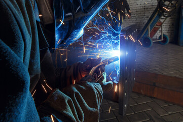 A worker welds in an industrial area. Welding arc close-up.