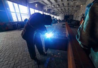 A worker welds in an industrial area. Welding arc close-up.