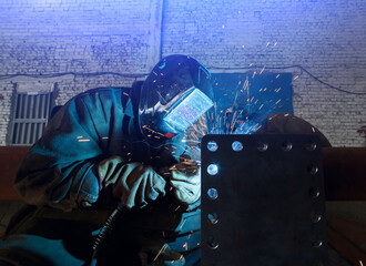 A worker welds in an industrial area. Welding arc close-up.
