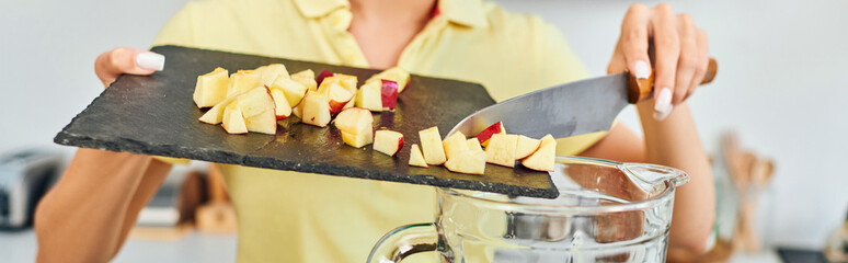 partial view of vegetarian woman adding ripe chopped apple in electric blender, horizontal banner
