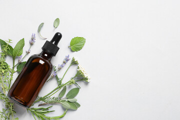 Bottle of essential oil, different herbs and flowers on white background, flat lay. Space for text