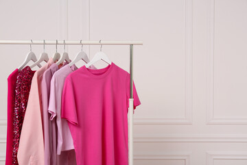 Rack with different stylish women`s clothes near white wall, space for text