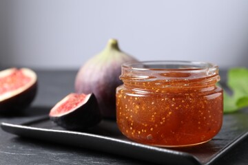 Jar of tasty fig jam and fresh fruits on black table, closeup. Space for text