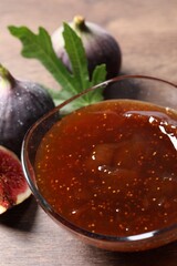 Glass bowl with tasty sweet jam and fresh figs on wooden table, closeup