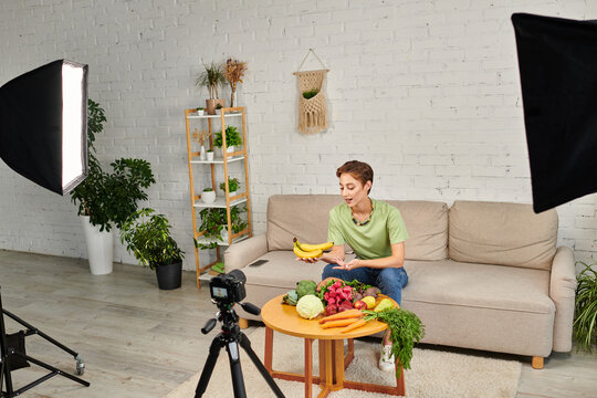 Woman With Ripe Bananas Talking Near Fresh Plant Origin Food And Digital Camera In Green Living Room