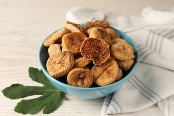 Bowl with tasty dried figs and green leaf on white wooden table