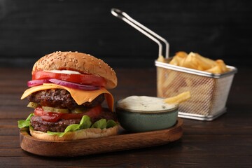 Tasty cheeseburger with patties, tomato and sauce on wooden table