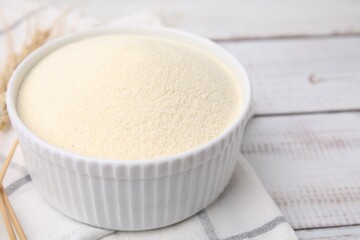 Uncooked organic semolina in bowl on white wooden table, closeup. Space for text