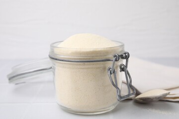 Uncooked organic semolina in jar and spoon on white tiled table, closeup