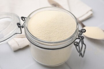 Uncooked organic semolina in jar on white tiled table, closeup