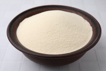 Uncooked organic semolina in bowl on white tiled table, closeup