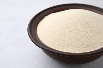 Uncooked organic semolina in bowl on white tiled table, closeup. Space for text