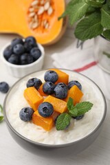 Bowl of delicious rice porridge with blueberries, pumpkin and mint on table, closeup