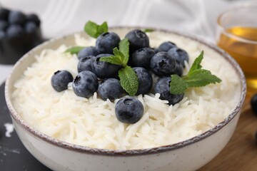 Bowl of delicious rice porridge with blueberries and mint on table, closeup