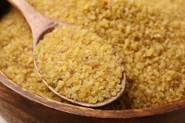 Wooden bowl and spoon with raw bulgur, closeup