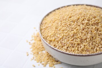 Raw bulgur in bowl on white table, closeup. Space for text