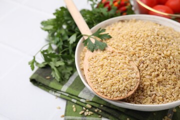Bowl and spoon with raw bulgur on table, closeup