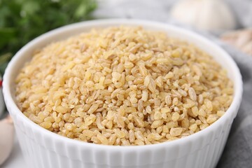 Raw bulgur in bowl on table, closeup