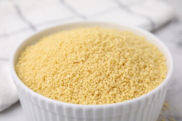 Raw couscous in bowl on light table, closeup