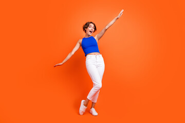 Full body photo of gorgeous overjoyed lady raise hands dancing good mood isolated on orange color background