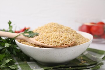 Bowl and spoon with raw bulgur on table, closeup