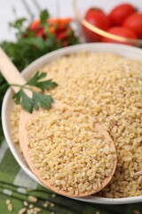 Bowl and spoon with raw bulgur on table, closeup