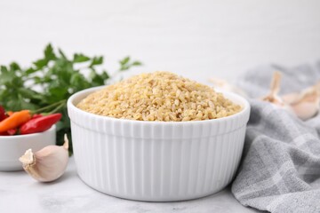 Raw bulgur in bowl and spices on table, closeup