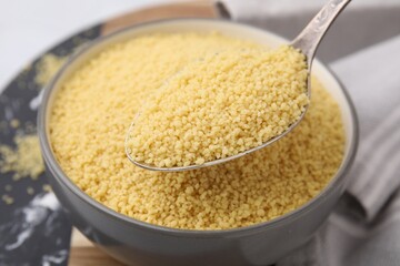 Taking raw couscous with spoon from bowl, closeup