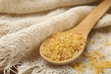 Wooden spoon with raw bulgur on beige cloth, closeup