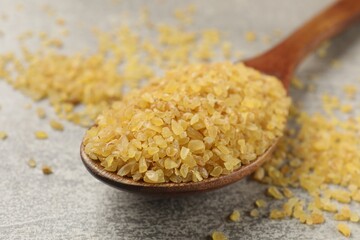 Spoon with raw bulgur on gray table, closeup