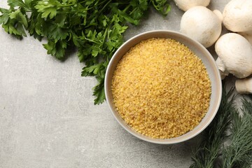 Raw bulgur in bowl, herbs and mushrooms on gray table, flat lay. Space for text