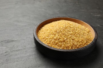 Raw bulgur in bowl on dark gray table, closeup