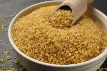 Bowl and scoop with raw bulgur on table, closeup