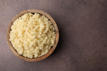 Tasty couscous in bowl on brown table, top view. Space for text