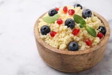 Bowl of tasty couscous with blueberries, pomegranate and mint on white marble table, closeup. Space for text