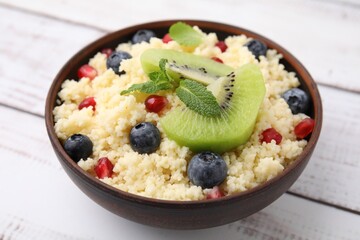 Bowl of tasty couscous with kiwi, blueberries and pomegranate on white table, closeup