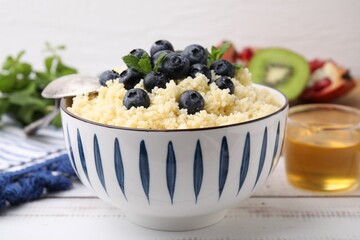 Bowl of tasty couscous with blueberries and mint on white table, closeup