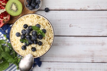 Bowl of tasty couscous with blueberries and mint served on white wooden table, flat lay. Space for...