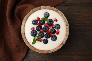 Bowl of delicious semolina pudding with blueberries, pomegranate and mint on wooden table, top view