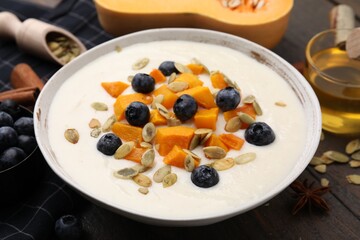 Bowl of delicious semolina pudding with blueberries, pumpkin and seeds on table, closeup