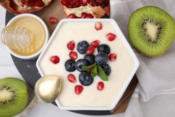 Bowl of delicious semolina pudding with blueberries, pomegranate and mint served on table, flat lay