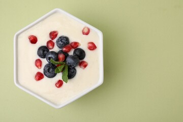 Bowl of delicious semolina pudding with blueberries, pomegranate and mint on light green background, top view. Space for text
