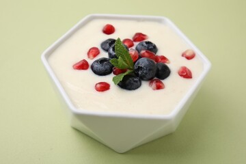 Bowl of delicious semolina pudding with blueberries, pomegranate and mint on light green background, closeup