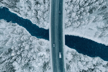 Aerial top view of snow winter road with cars over blue river - Powered by Adobe