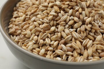 Dry pearl barley in bowl on white table, closeup