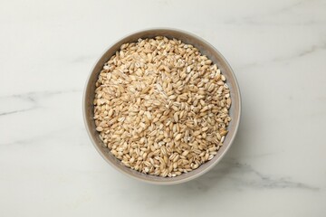 Dry pearl barley in bowl on white marble table, top view