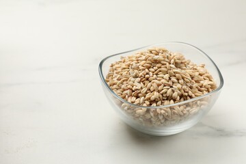 Dry pearl barley in bowl on white marble table, space for text