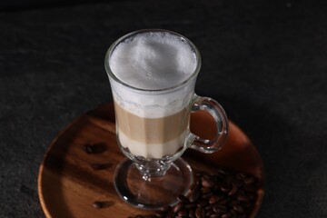 Aromatic latte macchiato in glass and coffee beans on dark grey table, closeup