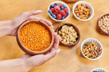 cropped woman with bowl of lentils near various berries and nuts on table at home, plants-based diet
